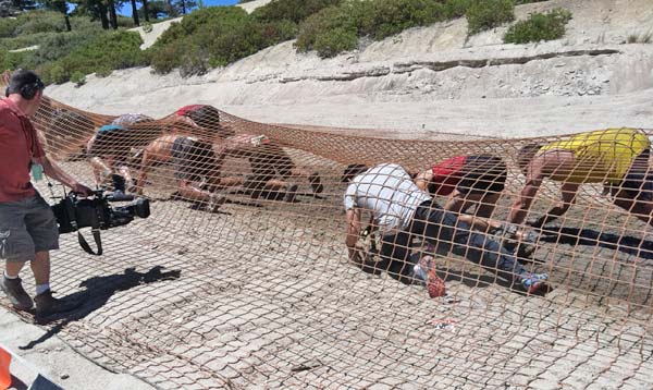 Tough Mudder participants crawl underneath a net...