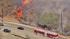 Cars are seen driving past a brush fire that...