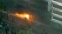 People throw objects at a fire at the base of a...