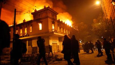 Protesters pass by a burning cinema in Athens, Sunday, Feb. 12, 2012.