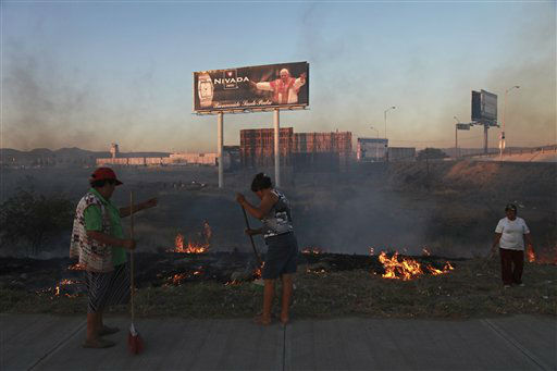 Women sweep an area by a field where billboards from a watch company welcome Pope Benedict XVI near the airport in Leon, Mexico, Thursday March 22, 2012.