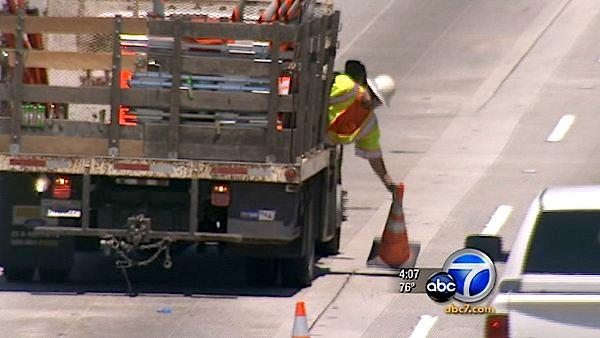 A worker reaches to pick up cones blocking lanes on the 405 Freeway in preparation to reopen Sunday, July 17, 2011.
