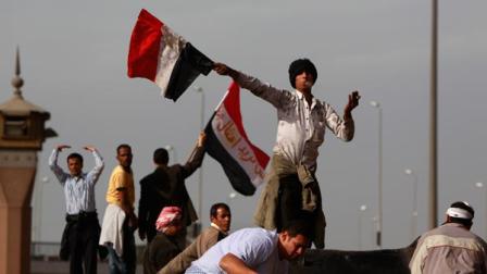 An anti-government protester swings an Egyptian flag, while smoking a cigarette, to beckon others to reinforce those at the frontline of clashes with pro-government supporters, near the Egyptian Museum in downtown Cairo