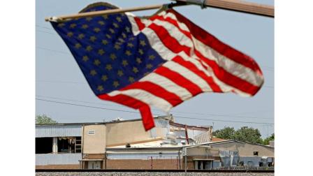 Five days after a fertilizer plant explosion, a flag flies from a damaged home as the damaged West Intermediate School is seen in the distance Monday, April 22, 2013, in West, Texas.