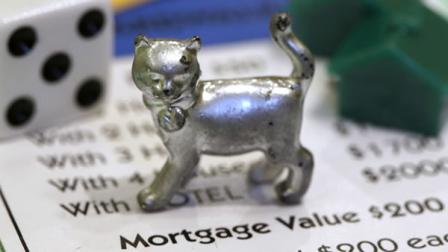 The newest Monopoly token, a cat, rests on a Boardwalk deed next to a die and houses at Hasbro Inc. headquarters, in Pawtucket, R.I., Tuesday, Feb. 5, 2013. Voting on Facebook determined that the cat would replace the iron token. (AP Photo/Steven Senne)