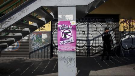 A sign that reads in Spanish For your family: Voluntary disarmament advertises a government program that exchanges peoples guns for things like bicycles, computers, tablets and money.