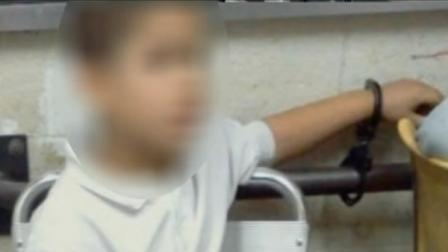 A young boy sits handcuffed to a bar in a New York City police precinct.