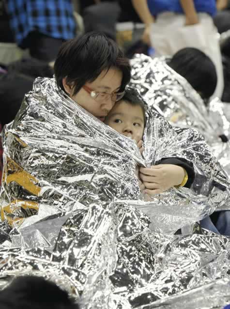 A child is held by a woman in a disaster sheet...