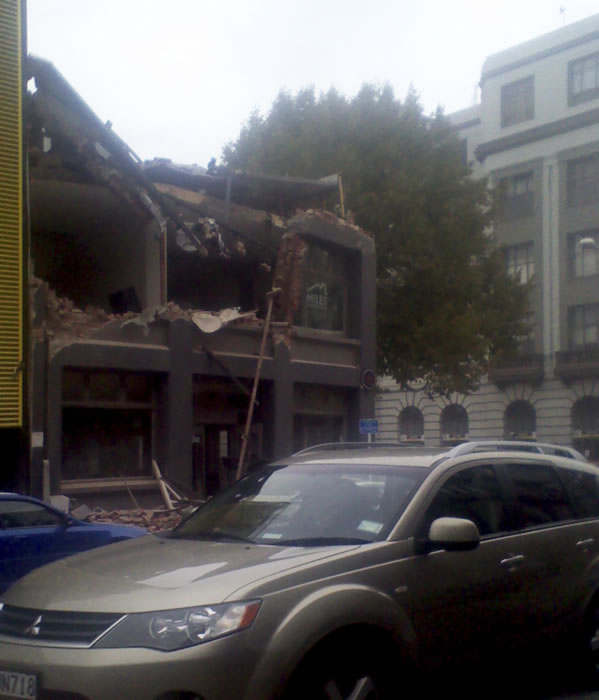 A car drives past a destroyed building in...