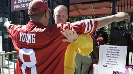 a stadium security officer pats down a football fan