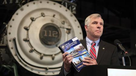 Standing in front of an old steam locomotive, Tom Unberg, chairman of the California High-Speed Rail Authority displays a copy of the systems new business plan during a news conference at the California Railroad Museum.