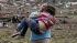 A woman carries her child through a field near the collapsed Plaza Towers Elementary School in Moore, Okla., Monday, May 20, 2013.