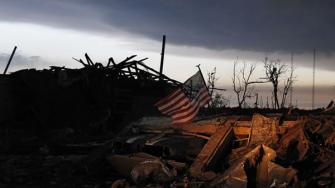 At sunrise Tuesday May 21, 2013, an American flag blows in the wind atop the rubble of a destroyed home in Moore, Okla.