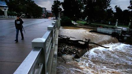 A woman walks past Boulder Creek, whose swollen waters have receded somewhat since the intense rain which had fallen for days has abated over the past two days, in Boulder, Colo., Sunday, Sept. 15, 2013