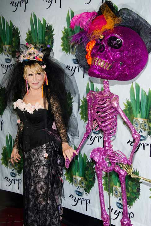 Bette Midler poses alongside a skeleton statue...
