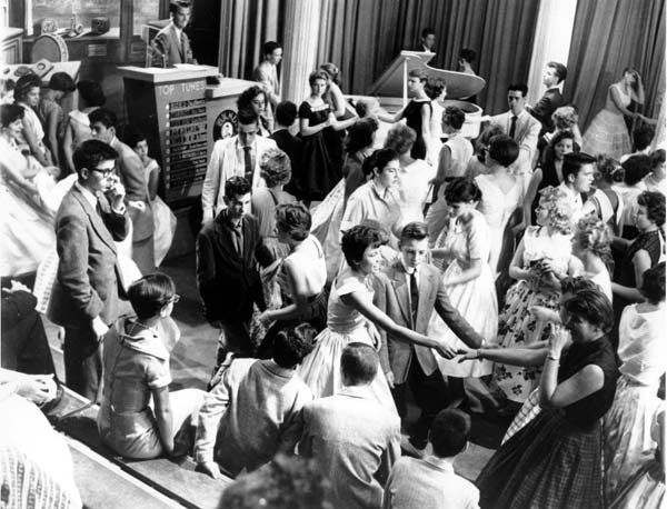 Disc jockey Dick Clark at podium at upper left is surrounded by teenage 