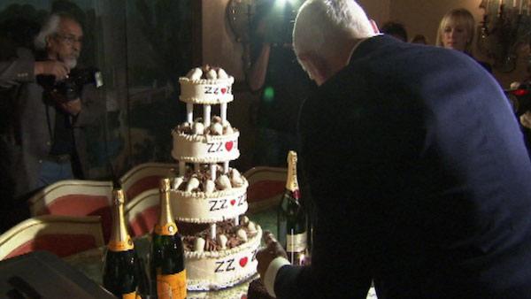 Frederic Prinz von Anhalt bends over a square chocolate cake made by Wolfgang Puck for his wife Zsa Zsa Gabor at the ailing actress' 95th birthday party on Feb. 6, 2012. Next to him is a four-tier cake and champagne bottles.