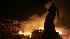 A building burns behind a statue of Madame Colot...