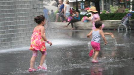 A girl and boy run and play in the water at Millennium Park.