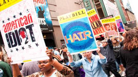 In this 2010 image released by Boneau Bryan Brown, people parade autographed Playbill posters of Broadway productions during the Broadway Cares equity Fights AIDS flea market and auction in New York. The annual Broadway Flea Market and Grand Auction celebrates its 25th year on Sunday, offering items far from the typical knickknacks elsewhere: a meeting with Bernadette Peters backstage at Follies; the chance to see The Book of Mormon and meet the stars; being part of the wedding scene onstage at Mamma Mia!