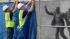Workers place a tarp on a fence in front of the...