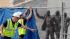 Workers place a tarp on a fence in front of the...