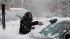 A woman clears snow from her parked car...