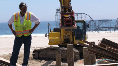 In this May 10, 2013 photo, a supervisor watches work crews rebuilding a section of the boardwalk in Seaside Heights, N.J. The Jet Star roller coaster that plunged off a pier into the ocean during Superstorm Sandy is visible in the background. Jersey shore towns up and down the coast are racing to finish rebuilding their boardwalks in time for Memorial Day weekend and the arrival of tourists in two weeks. (AP Photo/Wayne Parry)