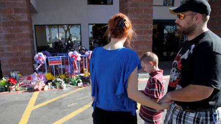Tom LaCorte, right, and his wife Ana LaCorte, of Tucson, Ariz., with their son Tommy LaCorte, all pause for a moment as they look at a makeshift memorial at a Safeway grocery store, opened for the first time since a mass shooting of 19 people that left six dead the previous Saturday, on Saturday, Jan. 15, 2011, in Tucson, Ariz. One of the injured gunshot victims was Rep. Gabrielle Giffords, D-Ariz., who is still in critical condition, was one of 19 victims shot on Saturday. (AP Photo/Ross D. Franklin)