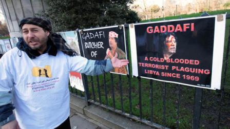 A Libyan activist talks next to posters depicting Libyan leader Muammar Gaddafi, during a protest against his rule by activists from the British Libyan Solidarity Campaign, across the street from the Libyan embassy in London, Tuesday Jan. 18, 2011.