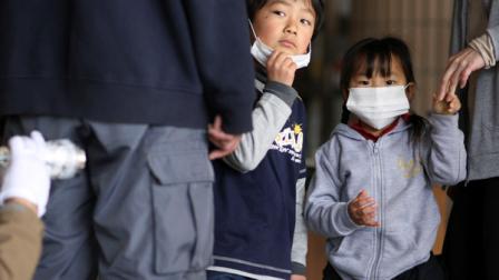 Children watch their father is screened for radiation at a shelter, Tuesday, March 29, 2011, in Fukushima, Fukushima prefecture, Japan. Highly toxic plutonium is seeping from the damaged nuclear power plant in Japans tsunami disaster zone into the soil outside, officials said Tuesday, further complicating the delicate operation to stabilize the overheated facility.