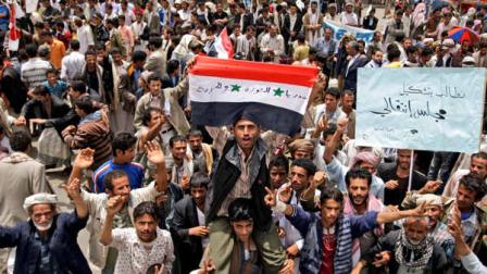 An anti-government protestor, center, holds a Syrian flag that reads in Arabic, Syria, revolution, and freedom, during a demonstration demanding the resignation of Yemeni President Ali Abdullah Saleh, in Sanaa, Yemen, Tuesday, June 14, 2011. A senior Yemeni official in the Saudi capital says President Ali Abdullah Saleh has developed a problem with his throat but that his overall condition is stable. Arabic reads on the placard right, We demand the formation of a transitional council.