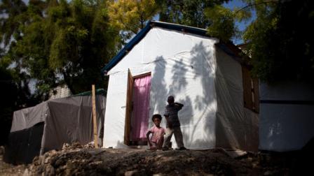 In this photo taken June 20, 2011, children look at the camera in front of their temporary house at a refugee camp set up for people displaced by the January 2010 in Carrefour, Port-au-Prince, Haiti. The structure is one of hundreds of wooden frames with steel or plywood roofs that foreign aid groups erected as a temporary fix for people displaced by the January 2010 earthquake, a way station between squalid tent camps and the new homes that would one day be built for the displaced. (AP Photo/Ramon Espinosa)