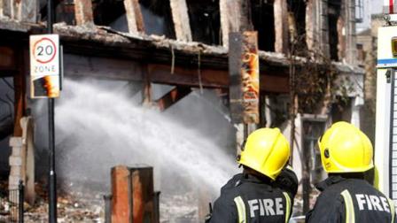Firefighters look at a burned-out building in Tottenham, north London, Sunday, Aug. 7, 2011, still being damped down after a demonstration against the death of a local man turned violent and cars and shops were set ablaze. One police officer was hospitalized and seven others were injured during riots after a north London suburb exploded in anger Saturday night following a gathering to protest the Thursday shooting by police of the 29-year-old.