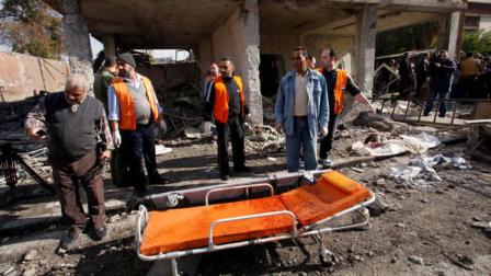 People stand at the site of a suicide bombing in Damascus, Syria, Friday, Dec. 23, 2011. A Syrian military official says the death toll from twin suicide car bombings in Damascus is now more dozens. The military official says more than a hundred people were wounded in the explosions targeting security and intelligence headquarters in the Syrian capital.
