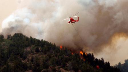Flames of the Waldo Canyon Fire races down into western portions of Colorado Springs, Colo. on Tuesday, June 26, 2012. A helicopter tries to slow it down before it left a trail of destruction, burning homes and buildings in its path. Heavily populated areas in the fires path have been affected. (AP Photo/Bryan Oller)