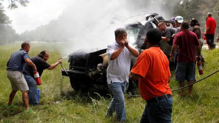 Passers-by rescue a woman pinned in a burning car on Interstate 10 in Hancock County, Miss., Thursday, Aug. 16, 2012. The fire was extinguished by the hose of a cement mixer, and fire extinguishers from nearby 18 wheelers. The woman was then extracted from the wreckage by the civilians as rescue personnel arrived, and she and her handicapped child, who was removed from the wreckage early, were airlifted from the scene. (AP Photo/Gerald Herbert)