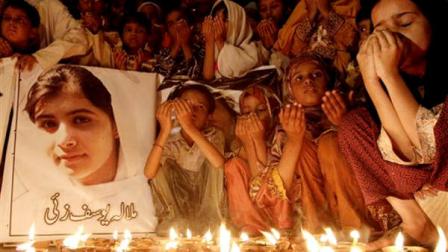 Pakistani children pray for the recovery of 14-year-old schoolgirl Malala Yousufzai, who was shot on Tuesday by the Taliban for speaking out in support of education for women, during a candlelight vigil in Karachi, Pakistan, Friday, Oct. 12, 2012. A Pakistani military spokesman says Yousufzai is in satisfactory condition but cautions that the next few days will be critical. Writing reads on the poster left, Malala Yousufzai.(AP Photo/Shakil Adil)
