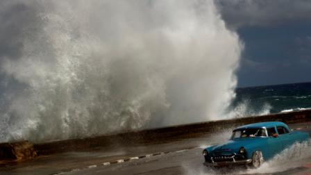 A driver maneuvers his classic American car along a wet road as a wave crashes against the Malecon in Havana, Cuba, Thursday, Oct. 25, 2012. Hurricane Sandy blasted across eastern Cuba on Thursday as a potent Category 2 storm and headed for the Bahamas after causing at least two deaths in the Caribbean. (AP Photo/Ramon Espinosa)