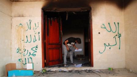 FILE - On this Wednesday, Sept. 12, 2012 file photo, a man looks at documents at the U.S. consulate in Benghazi, Libya, after an attack that killed four Americans, including Ambassador Chris Stevens. The graffiti reads, no God but God, God is great, and Muhammad is the Prophet. (AP Photo/Ibrahim Alaguri, File)