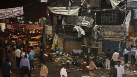 People and police officers stand at the spot after a bomb blast in Hyderabad, India, Thursday, Feb. 21, 2013. A pair of bombs exploded Thursday evening in a crowded shopping area in the southern Indian city of Hyderabad, killing several people and wounding many in the worst bombing in the country in more than a year, officials said. (AP Photo/Mahesh Kumar A.)