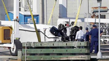 Members of the U.S. Coast Gard examine a small white boat, Wednesday, Oct. 16, 2013 at the U.S. Coast Guard Station Miami Beach, in Miami Beach, Fla. Four women died and 10 people were taken into custody after the boat with more than a dozen people aboard, including Haitian and Jamaican nationals, capsized early Wednesday in the waters off South Florida. It was overloaded and lacked lifejackets, according to the Coast Guard. (AP Photo/Wilfredo Lee)