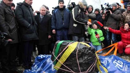 People look at what scientists believe to be a chunk of the Chelyabinsk meteor, recovered from Chebarkul Lake near Chelyabinsk, about 1500 kilometers (930 miles) east of Moscow, Russia, Wednesday, Oct. 16, 2013. Scientists on Wednesday recovered what could be the largest part of this meteor from Chebarkul Lake outside the city. They weighed it using a giant steelyard balance, which displayed 570 kilograms (1,256 pounds) before it broke. (AP Photo/Alexander Firsov)