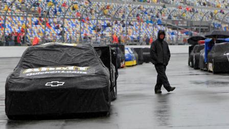 An crew member walks past race cars covered to protect them from the rain before the NASCAR Daytona 500 Sprint Cup series auto race at Daytona International Speedway in Daytona Beach, Fla., Sunday, Feb. 26, 2012. (AP Photo/John Raoux)