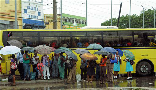 Commuters wait at a bus stop as rain brought by...