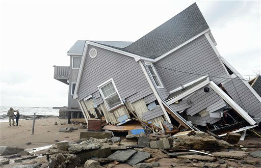 People stand next to a house collapsed from...